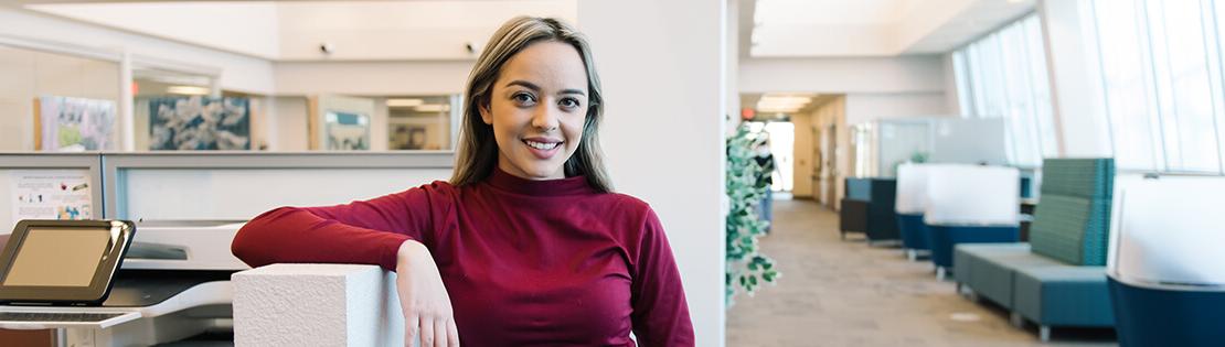 A student poses and smiles in a study area at a campus